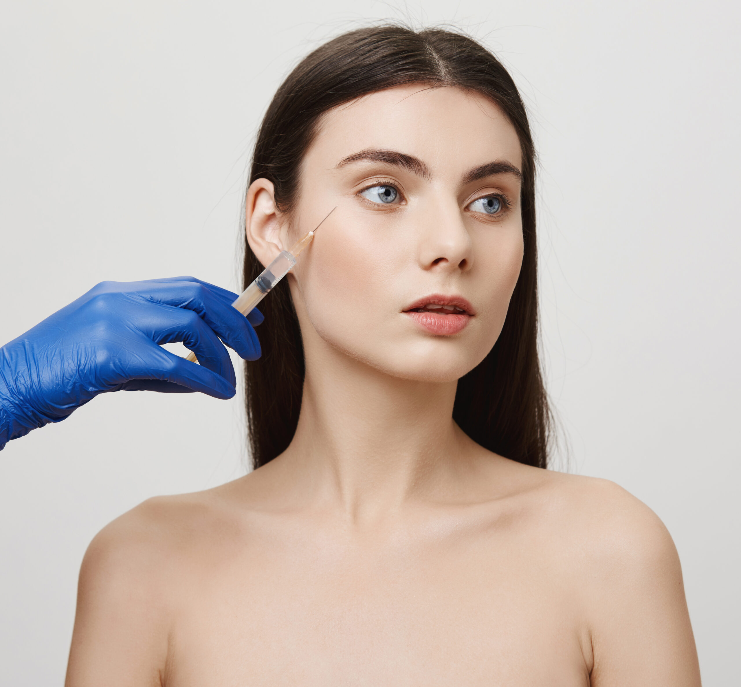 Wrinkles have no chance to exist on this face. Portrait of focused attractive woman standing naked while cosmetologist make injection in cheek for cosmetic purpose, being careful and professional.